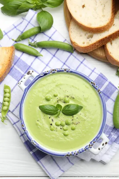 Beyaz ahşap masada servis edilen fesleğenli bezelye kremalı çorba.