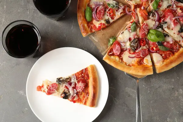 Gri masada servis edilen ince tütsülenmiş sosisli lezzetli bir pizza.