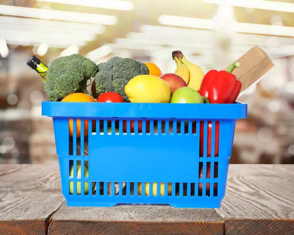 Süpermarketteki ahşap masada içi alışveriş sepetiyle dolu mavi alışveriş sepeti.