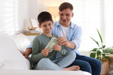 Baba, evdeki kanepede oğluna harçlık veriyor.