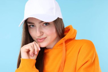 Açık mavi arka planda şık beyzbol şapkalı güzel bir kadının portresi, yakın plan.