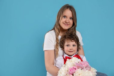 Küçük çocuk açık mavi arka planda annesine güzel şakayık çiçekleri veriyor. Metin için boşluk