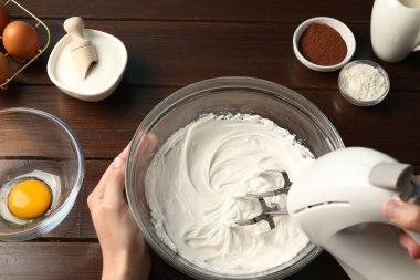 Ahşap masada el çırpıcı kremalı bir kadın.