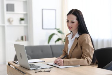 Ofiste dizüstü bilgisayarla çalışırken not alan profesyonel bir psikolog.