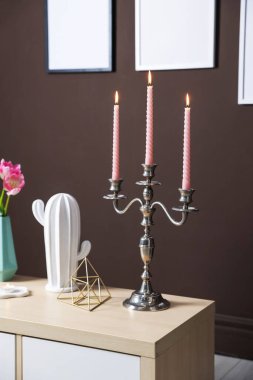 Kahverengi duvarın yanındaki dolapta yanan mumlar ve dekorlar olan zarif bir şamdan.