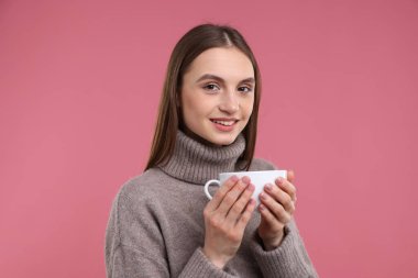 Pembe arka planda bir fincan kahveyle gülümseyen kadın.