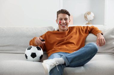 Uzaktan kumandalı futbol fanatiği ve kanepede maç izleyen futbol topu.