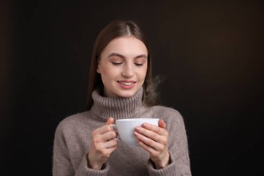 Kahverengi arka planda bir fincan kahveyle gülümseyen kadın.