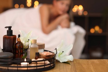 Üst düzey kadın masaj koltuğunda dinleniyor, farklı spa ürünlerine ve zambak çiçeklerine odaklanıyor.