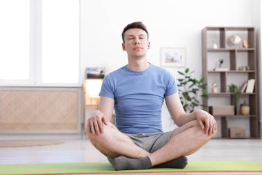 Genç adam evde yoga yapıyor.