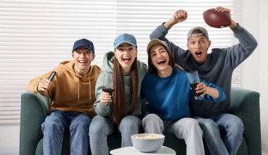 Duygusal sporseverler kanepede kapalı alanda maç izliyorlar.