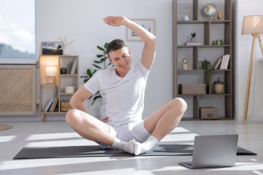 Evde bilgisayarla yoga dersi alan bir adam.