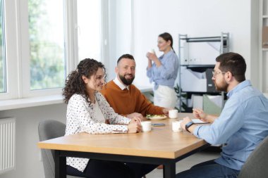 İş arkadaşları ofiste yemek yiyor ve sohbet ediyorlar.