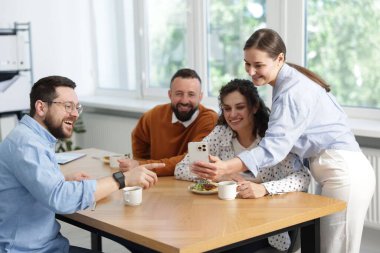 Ofiste öğle arasında iş arkadaşlarına akıllı telefondan bir şey gösteren bir kadın.