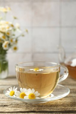 Cam bardakta nefis papatya çayı ve ahşap masada taze çiçekler, yakın plan.