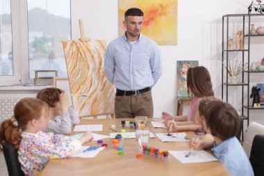 Çocuklara resim dersinde resim yapmayı öğreten bir adam.