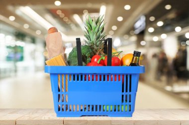 Süpermarketteki ahşap masada içi alışveriş sepetiyle dolu mavi alışveriş sepeti.