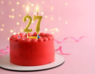 Pembe arka planda yanan mumlar, bulanık ışıklar ve mesaj için yer olan lezzetli bir pasta. 27. yaş günü veya başka özel bir gün.