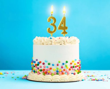 Yanan mumlar ve açık mavi arka planda serpiştirilmiş şekerlerle nefis bir pasta. 34. yaş günü veya diğer özel günler