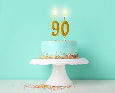 Turkuaz arka planda yanan mumlar ve beyaz masaya serpiştirilmiş lezzetli bir pasta. 90. yaş günü veya diğer özel günler