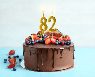 Meyveli çikolatalı kek ve açık mavi masada yanan mumlar. 82nci yaş günü veya diğer özel günler