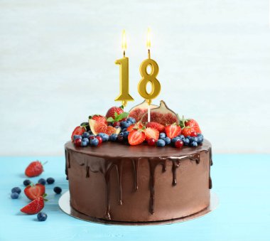 Meyveli çikolatalı kek ve açık mavi masada yanan mumlar. 18. yaş günü veya başka özel bir gün.