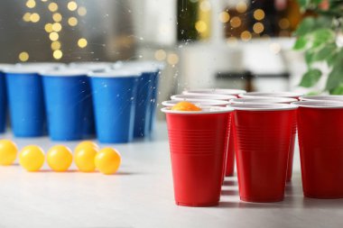 Aydınlık masada, bulanık ışıklara karşı plastik bardağa düşen turuncu top. Bira pong oyunu