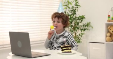 Little boy celebrating his birthday while having video call via laptop at table indoors