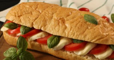 Bir kadın mozarella peyniri, domates ve fesleğenle lezzetli bir sandviç kesiyor.