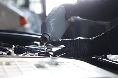 İşçi motor yağını teneke kutudan araba motoruna boşaltıyor.