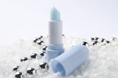 Nemlendirici dudak kremi ve yapay kar üzerine Noel süsü, yakın plan. Kış bakımı