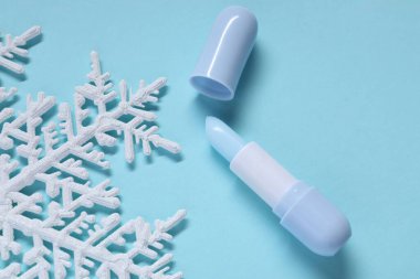 Nemlendirici dudak kremi ve açık mavi arka planda Noel dekoru, düz yatış. Kış bakımı