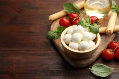 Lezzetli mozzarella peyniri topları, ekmek çubukları, domates ve ahşap masada fesleğen. Metin için boşluk
