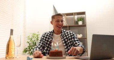 Doğum günü kutlaması. Adam pastaya mum üflerken içerideki masada dizüstü bilgisayarla görüntülü arama yapıyor.