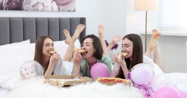 Pijama partisi. Mutlu arkadaşlar evde yatakta pizza yiyor.