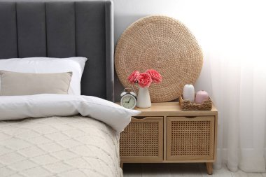 Yatağın yanında alarm saati ve dekorasyonu olan komodinin yanında.