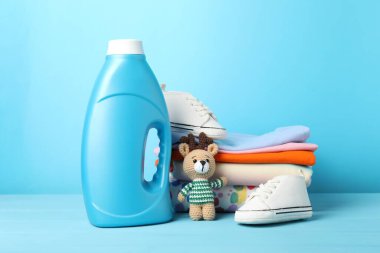 Şişe yumuşatıcı, bebek kıyafetleri ve açık mavi ahşap masada oyuncak.