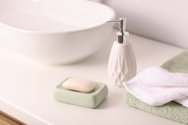 Sabun çubuğu, bir şişe kozmetik ürün ve kapalı alandaki beyaz tezgahta havlular, yakın plan.