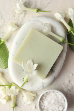 Bir kalıp sabun, deniz tuzu ve yasemin çiçekleri ışık masasında, düz yatıyordu.