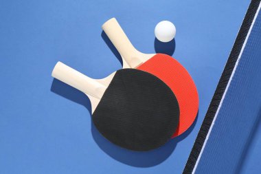 Masa tenisi raketleri, top ve ağ mavi arka planda, düz yatıyordu.