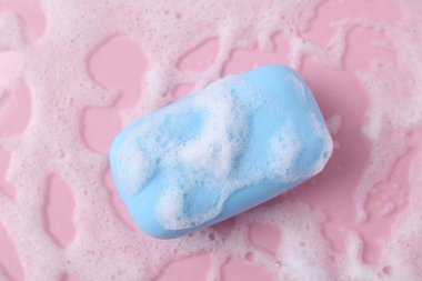 Pembe arka planda köpük olan sabun çubuğu, üst görünüm