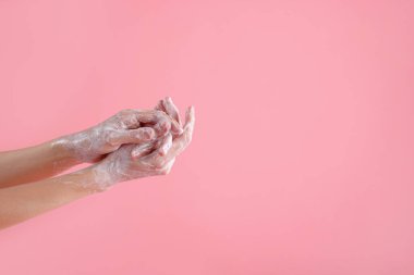 Açık pembe arka planda ellerini sabunla yıkayan kadın, yakın plan. Metin için boşluk