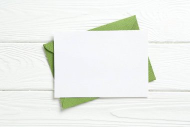 Beyaz ahşap masa üzerinde boş davetiye ve zarf, üst manzara. Tasarım için boşluk