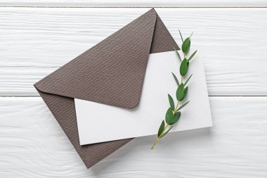 Boş davetiye kartı, zarf ve dal beyaz ahşap masa, üst görünüm