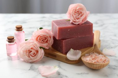 Sabun barları, kozmetik ürünleri ve beyaz mermer masada güzel güller, yakın plan.