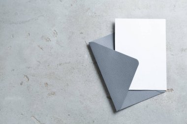 Açık gri masadaki boş davetiye ve zarf, üst manzara. Tasarım için boşluk