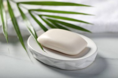 Sabun çubuğu, havlu ve palmiye yaprağı beyaz mermer masada, yakın plan.