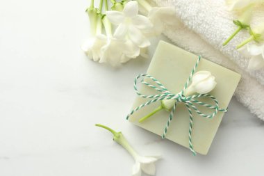 Bir kalıp sabun, yasemin çiçekleri ve beyaz mermer masa üzerinde havlu, düz. Metin için boşluk