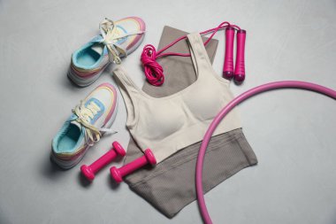 Spor kıyafetleri, spor ayakkabıları, hula hoop, ip atlama ve gri desenli arka planda dambıllar, düz uzanma