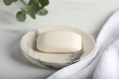 Sabun çubuğu, havlu ve okaliptüs dalı beyaz mermer masa üzerinde, yakın plan.